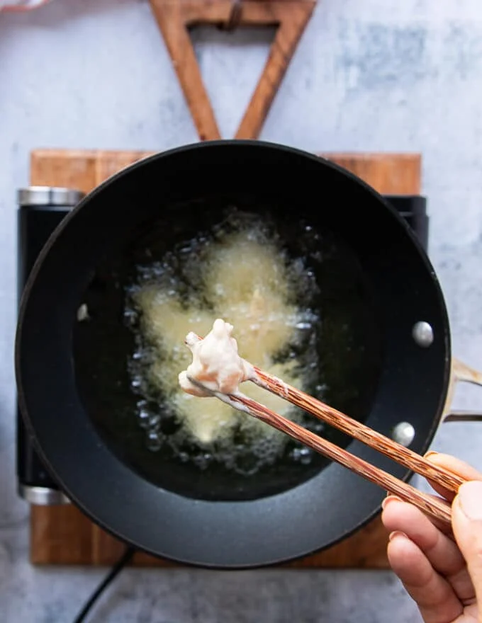 A hand holding chopsticks and adding the coated chicken one by one into the hot oil
