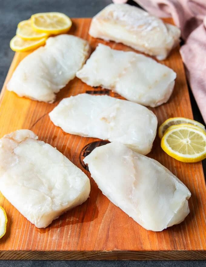 cod fish on a wooden board seasoned lightly with salt and pepper on both sides