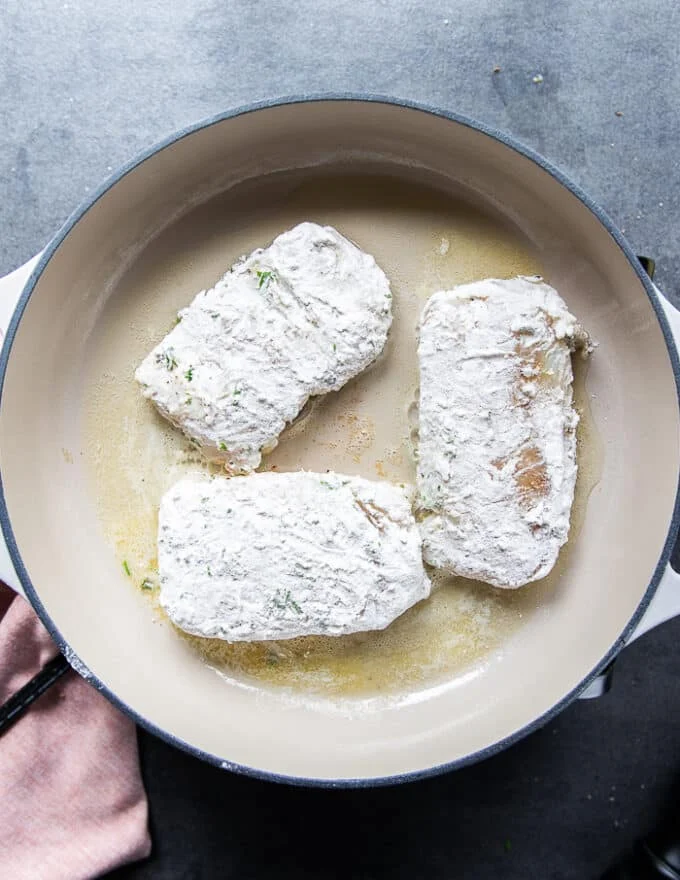 The cod fish coated in flour placed in a non stick skillets with butter