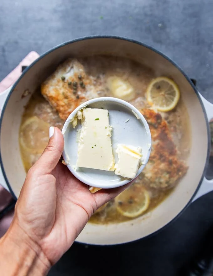 A hand holding a plate of cold butter pieces ready to add it into the sauce