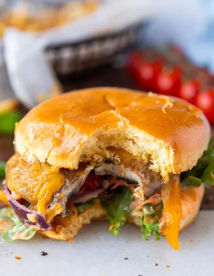 One bitten portobello mushroom burger showing the bite in the sandwich and a peak into the layers of the mushroom, sauce, toppings and melted cheese