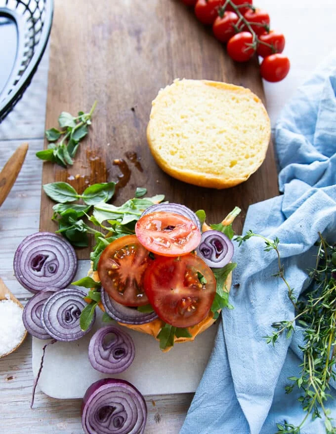 The toppings are loaded over the burger bun including some greens, sliced onions, sliced tomatoes