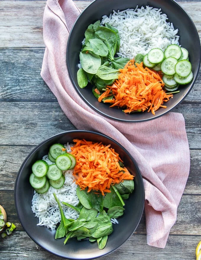 Shredded carrots, sliced cucumbers and avocados are arranged over the rice.