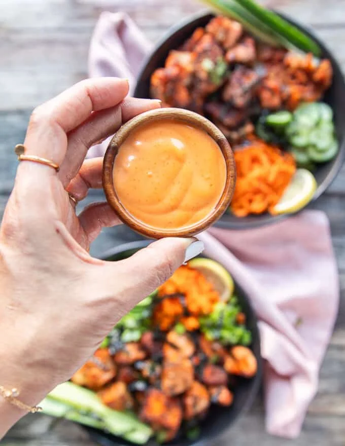 A hand holding a bowl of homemade spicy mayo ready to drizzle of the salmon bowls