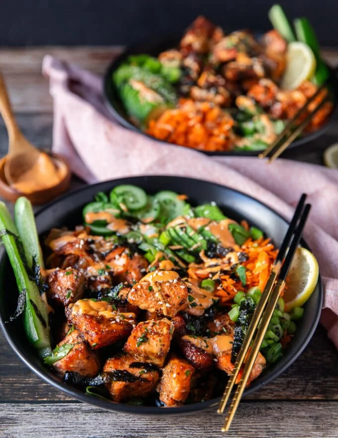 close up of aa salmon bowl showing the salmon loaded over rice, some seaweed, some carrots, cucumbers, avocado all arranged in the bowl and drizzled with spicy mayo