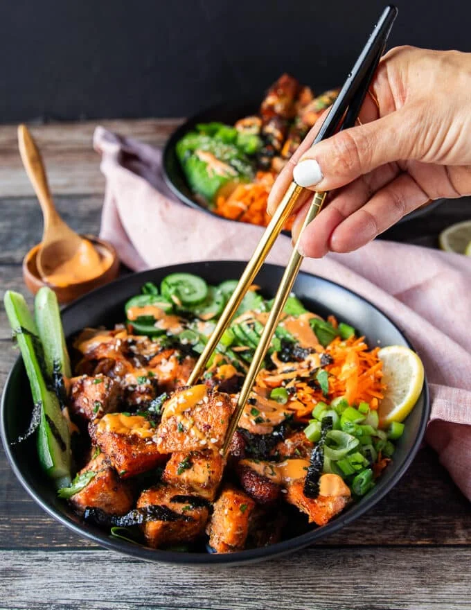 A hand using two chopsticks to grab a bite of the salmon bowls