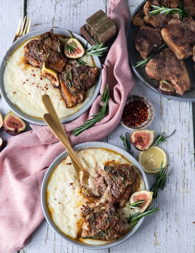 Two plates with lamb loin chops served over mashed potatoes and the rosemary butter on the side , some cutlery in one plate is showing how to eat the lamb loin chops