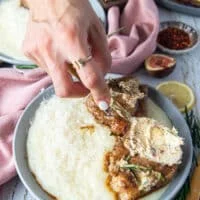 A hand using a spoon to spread some of the rosemary butter of each lamb loin chop and showing how the butter melts over the lamb