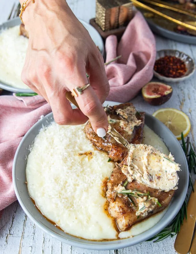 A hand using a spoon to spread some of the rosemary butter of each lamb loin chop and showing how the butter melts over the lamb