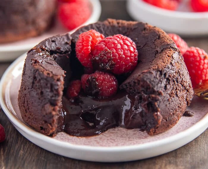 A molten lava cake broken in the middle showing the oozing chocolate center and some raspberries on the top