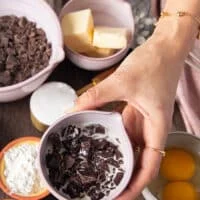 A hand holding the bowl of cream and chocolate chunks melted to form the truffle center of the lava cake recipe