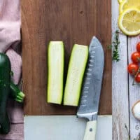 A zucchini cut in half on a wooden board using a sharp knife