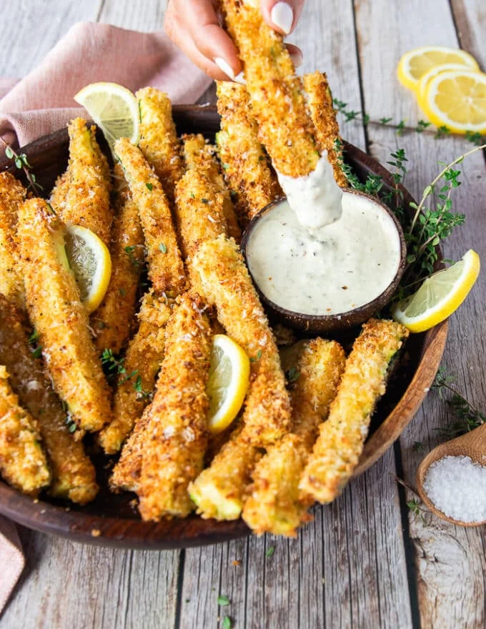 A hand dipping one zucchini fries into a garlic parmesan sauce