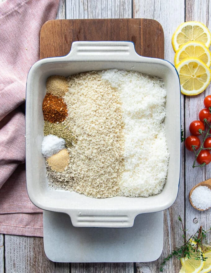 The best crisp coating ingredients for zucchini fries including a plate of panko bread crumbs, a bowl of parmesan cheese, and small bowls of garlic powder, oregano, paprika, onion powder and seasoning