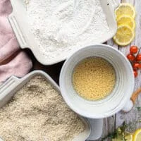 The breading station ready on a wooden board including the flour coating with the spices mixed in in a plate, the eggs beaten in a bowl and the panko coating with the spices and parmesan cheese mixed in a shallow plate