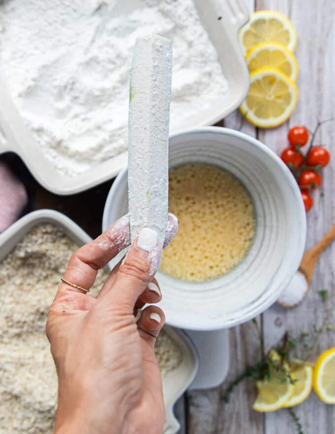 A hand holding the zucchini fries that has been dipped in the flour and shaken off.