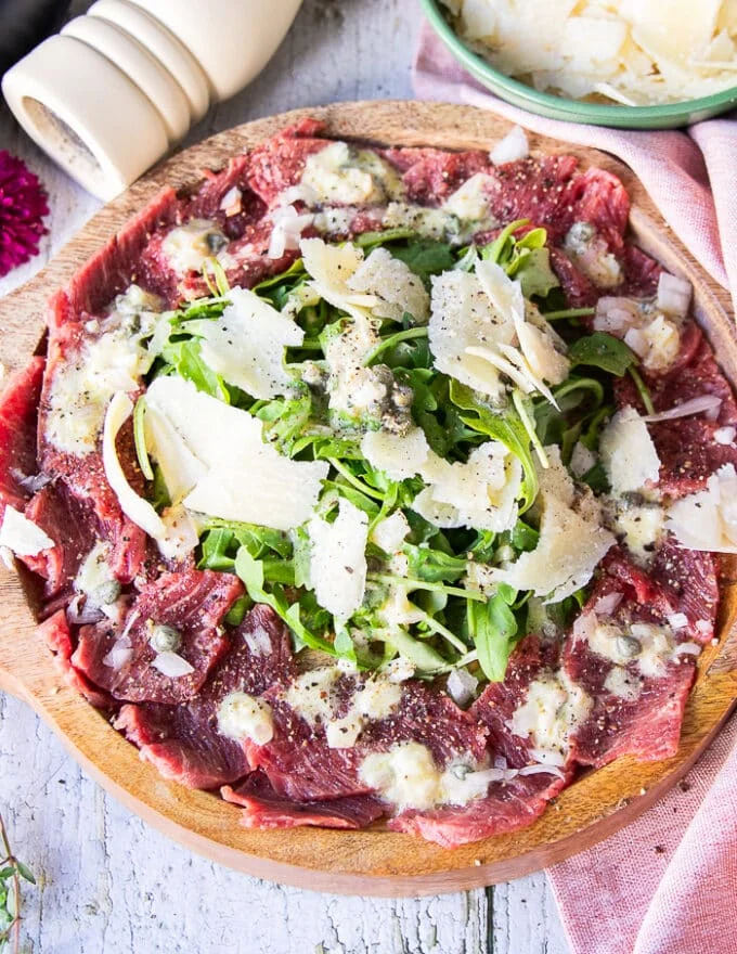 Fully dressed plate of beef carpaccio with the vinaigrette, the beef, arugula and parmesan shaving