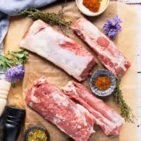 A set of lamb loin deboned and lamb sirloin and lamb tenderloin deboned on a parchment paper surrounded by a small bowl of chili flakes and some fresh thyme leaves