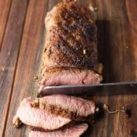 roasted lamb loin out of the oven, rested and a knife slicing it showing how perfectly cooked it is