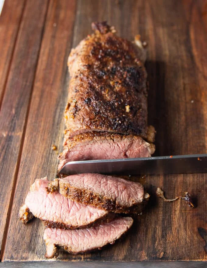 roasted lamb loin out of the oven, rested and a knife slicing it showing how perfectly cooked it is