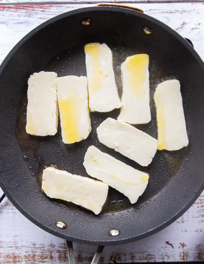 sliced halloumi in a skillet with olive oil searing