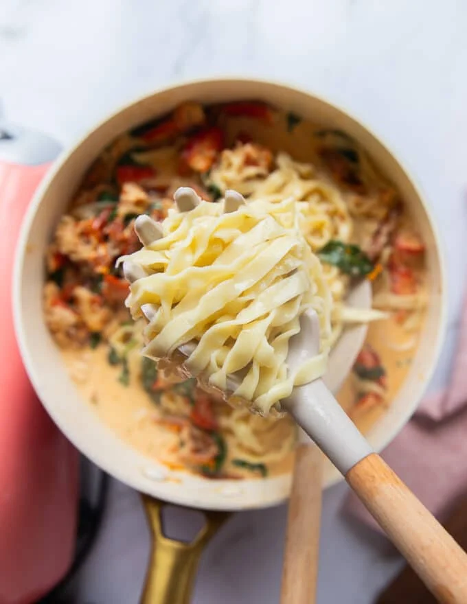 A pasta scoop adding in freshly cooked fettuccine into the creamy lobster sauce skillet