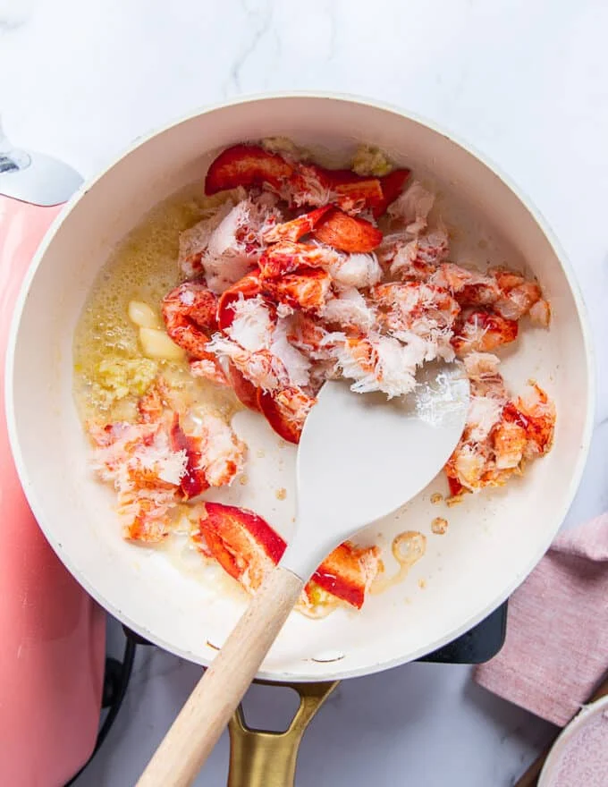 The lobster meat and garlic sautéing in a sauce pan in butter