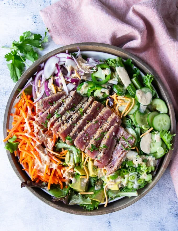 A full plate of dressed up ahi tuna salad with sesame dressing and the seared tuna on top sliced.