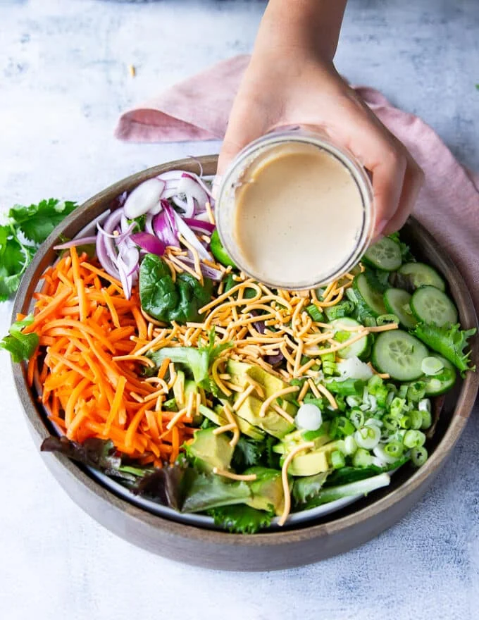 A hand pouring the sesame dressing over a bowl with the salad ingredients