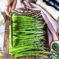 A hand holding a knife and trimming at the same point as the other snapped asparagus.