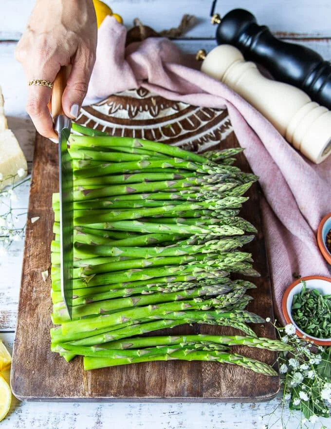 A hand holding a knife and trimming at the same point as the other snapped asparagus.