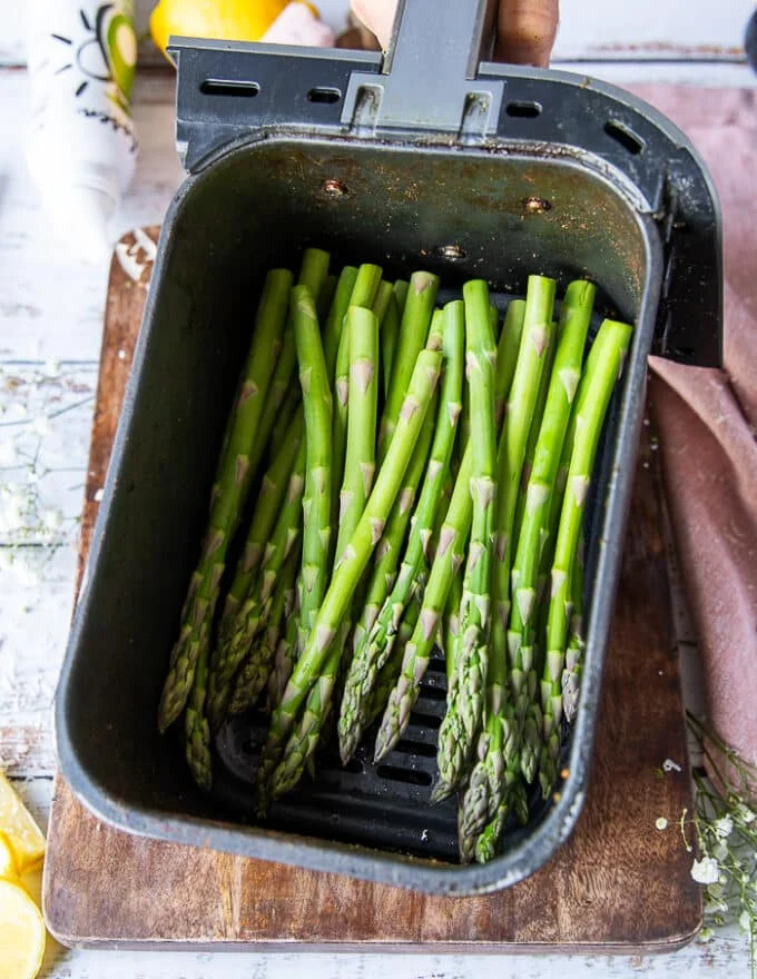 The trimmed asparagus placed in an air fryer basket sprayed with oil, salt and pepper.