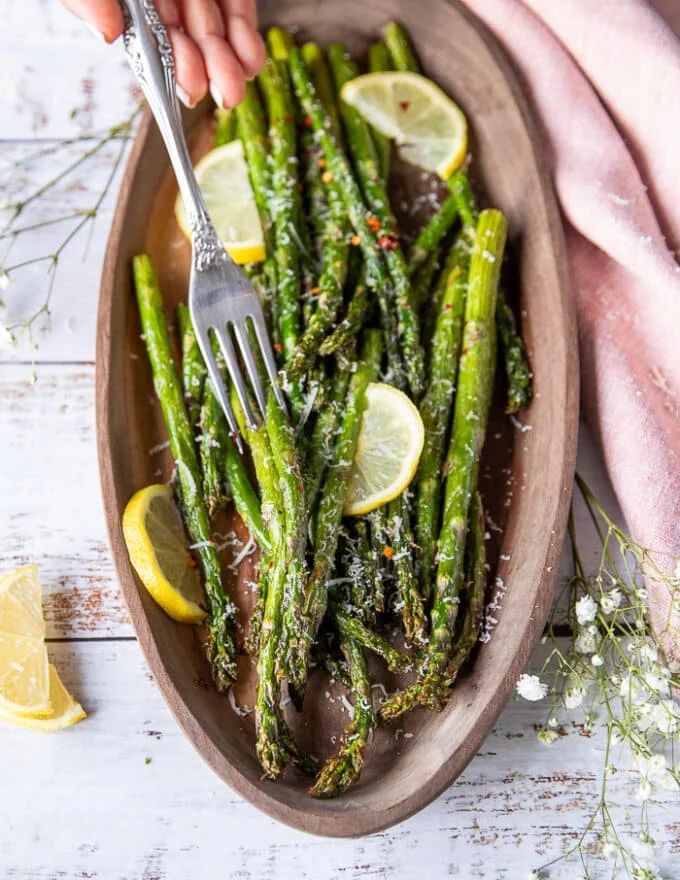 A hand using a fork to eat some air fryer asparagus showing the perfect texture close up and how well cooked it is