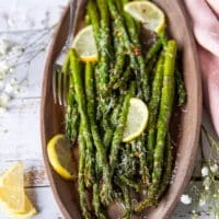 A plated Air fryer asparagus on a wooden plate with lemon slices and parmesan grated on top