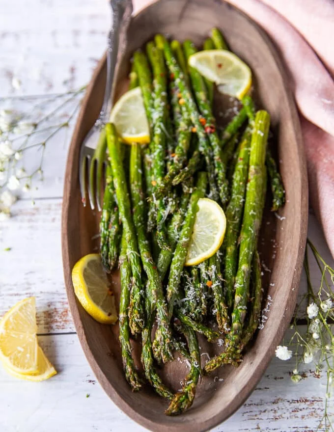 A plated Air fryer asparagus on a wooden plate with lemon slices and parmesan grated on top