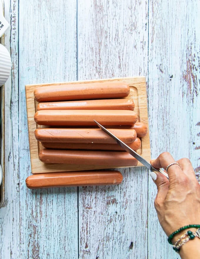 A hand holding a sharp knife and scorching the hot dogs on a diagonal to make like spirals on the side