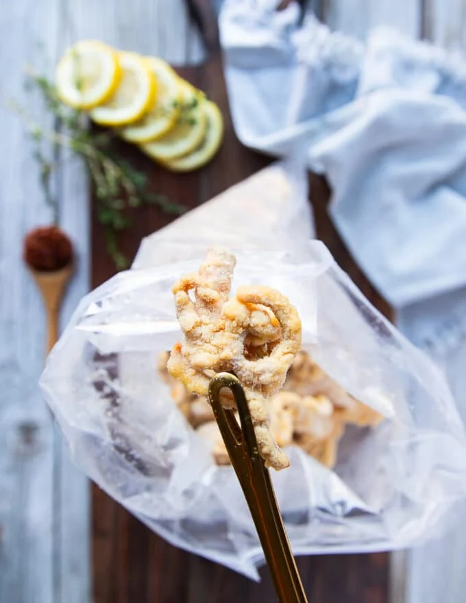 A hand holding a piece of battered shrimp up close to show the coating and it's ready for frying