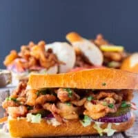 close up on a po boy sandwich cut in half , showing up close the fried shrimp and the sandwich toppings along with the sauce dripping on the sides of the bread