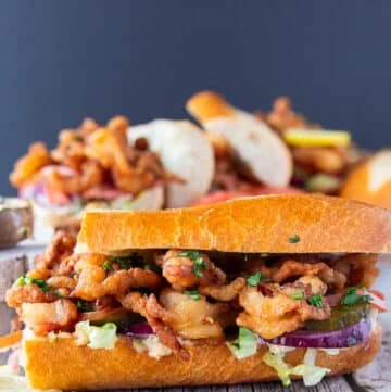 close up on a po boy sandwich cut in half , showing up close the fried shrimp and the sandwich toppings along with the sauce dripping on the sides of the bread