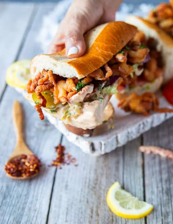 A hand dipping the po boy sandwich in extra spicy sauce