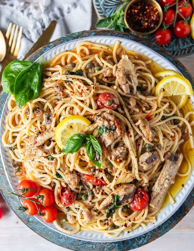 Tope view close up of the finished sardine pasta recipe showing the sardines, pasta, capers, tomatoes, olive oil, lemon zest and lots of lemon slices around