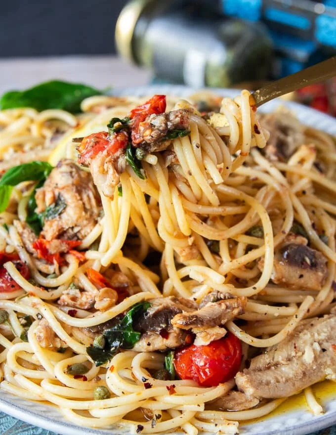 a fork stretching the sardine pasta close up showing the capers, sardines and saucy pasta recipe