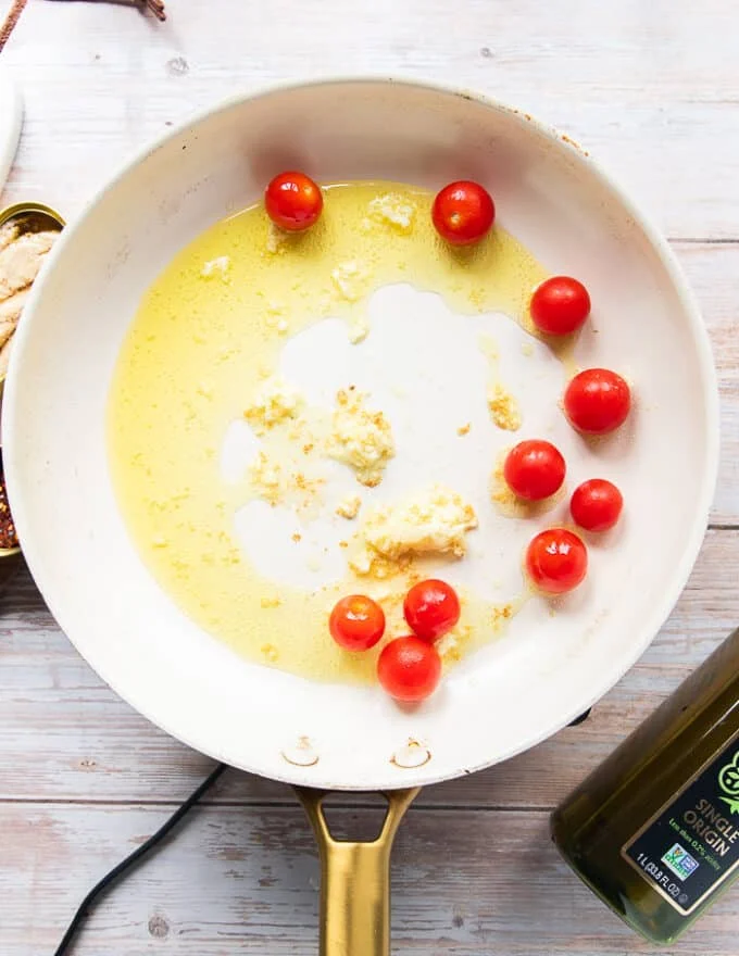 making sardine pasta sauce showing a skillets with lots of olive oil, garlic and cherry tomatoes cooking