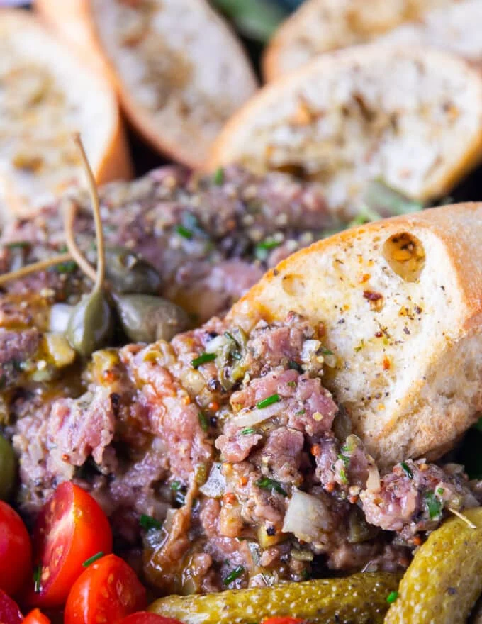 close up of a steak tartare broken up and served over a crunchy french baguette