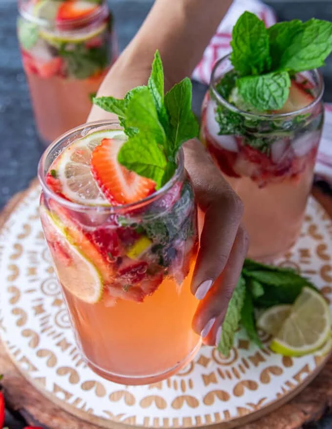 A hand holding a fully garnished cup of strawberry mojito close up showing the garnish, the drink