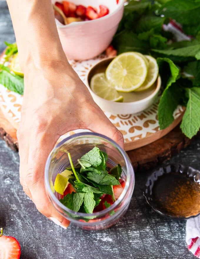 Lots of fresh mint, lime slices and honey is added to the strawberries at the bottom of the cup