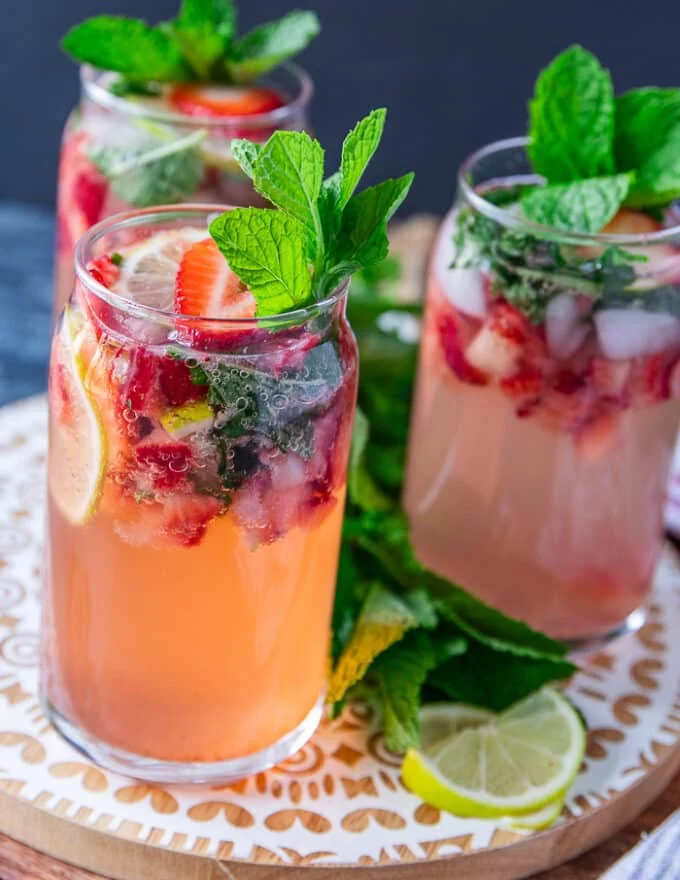 Close up on one strawberry mojito showing the crushed strawberries, lime slices and mint and garnished with more berries, mint and lime