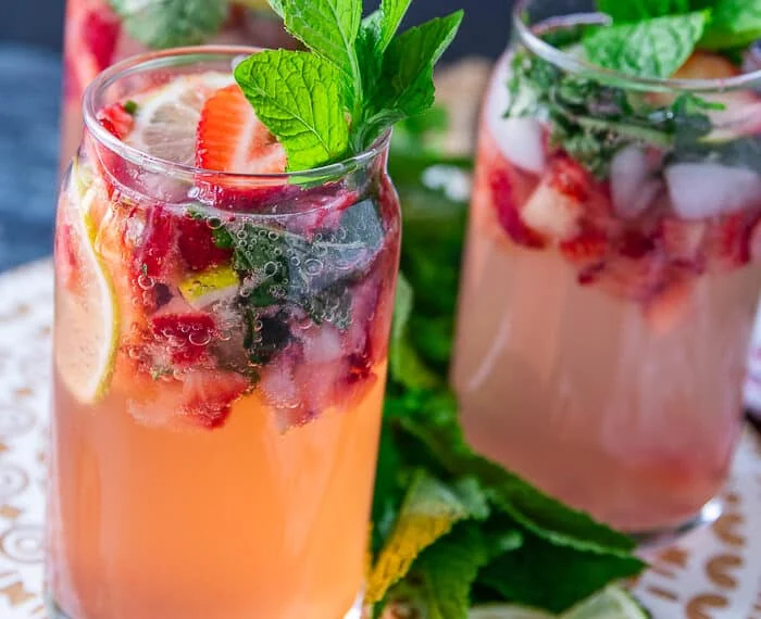 Close up on one strawberry mojito showing the crushed strawberries, lime slices and mint and garnished with more berries, mint and lime