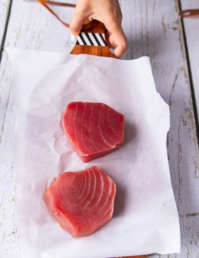 A hand holding a board with fresh ahi tuna steaks, and some fresh lettuce, avocado , onions