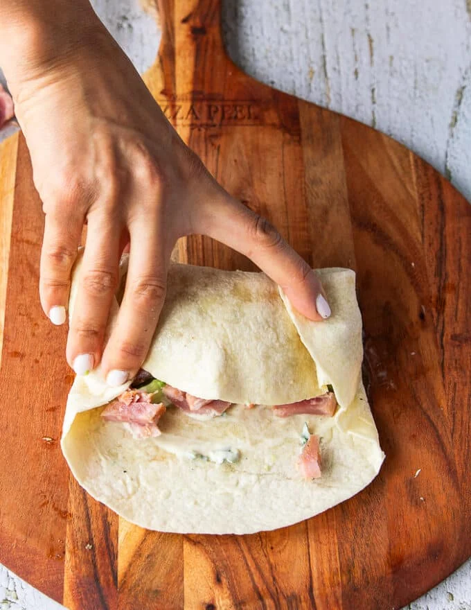 the second step and detailed how to fold a tortilla wrap is by folding in the corners to secure the filling inside.